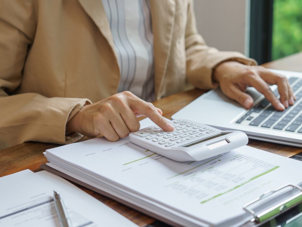 Utility Disconnection Guide Before Moving 4 Person calculating expenses related to utility disconnection on top of financial documents while working on a laptop at a wooden desk.